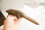 Hand holding the vintage African pangolin sculpture, displaying its length and carved scales.