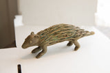 Vintage African porcupine sculpture in profile, highlighting the textured quills and aged green patina.