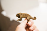 Side profile of a vintage African chameleon figurine held to show scale and handmade texture.