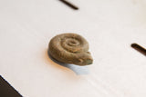 Side view of a vintage African curled snake figurine with rustic, aged patina.