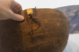 Hand holding antique carved wooden bowl rim, highlighting golden patch and leather loop.