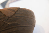 Storied metal staple repairs along the rim of the dark, incised wooden bowl.