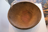 Antique hand carved wooden bowl's interior: textured brown surface, reddish highlights, and old repairs.