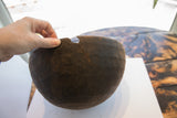 A hand holding the dark antique African carved wooden bowl's cracked, damaged rim.