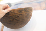 Aged texture and incised geometric patterns on an antique hand-carved wooden bowl.