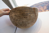 Hand holding antique African wooden bowl rim, revealing incised patterns and a prominent old repair.