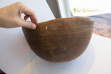 Hand holding antique African wooden bowl rim, showing incised lines and a circular repair.
