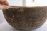 A hand gently touches the textured, dark wooden rim of an antique African bowl.
