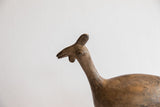 Profile view of the vintage African bird casting's head showing its simple form and aged texture.