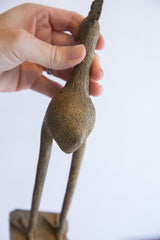 A hand holds the vintage African bird sculpture to detail its textured body and etched patterns.