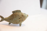 Side profile of a vintage cast fish showing its textured green patina and spiral etchings.