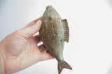 Hand holding vintage African fish casting with textured scales and distinctive spiral motifs.