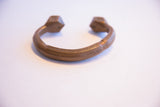 Curved copper band of an antique African bracelet with carved lines and faceted ends.