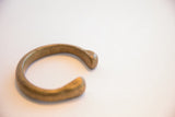 The smooth, rounded terminals of the antique brass cuff showing its aged patina.