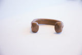 Rounded terminals with small stamped marks on an antique copper cuff.