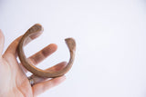 Antique African snake cuff bracelet held in a hand to show its scale and curved form.