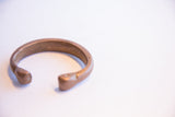 Side profile of the antique copper cuff showing its simple, curved form and patina.