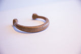 The warm, aged patina on the hand-formed curve of an antique African copper cuff.