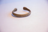 Side profile of an antique African bronze cuff showing its open shape and patina.