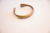 The C-shaped form and time-softened patina of the bronze snake cuff.