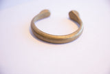The open C-shape and smooth, aged patina of the antique bronze bracelet.