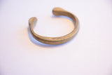 The solid, curved form of the bronze cuff with an age-softened patina.