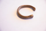 The simple, open C-shape of an antique African cuff bracelet with a darkened, aged patina.