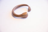 The smooth, patinated surface of the antique African snake cuff's stylized head.