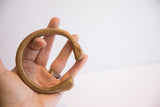The curved shape and antique brass patina of a snake cuff bracelet held in hand.