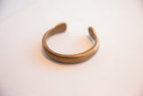 Angled view of an antique African snake cuff showing its curved shape and patterned surface.