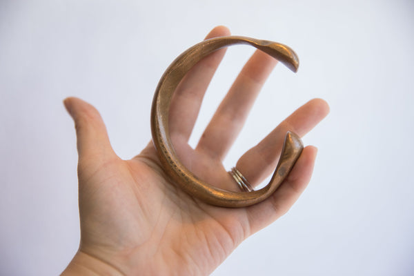 Hand holding an antique snake cuff, showing its solid form and aged patina.