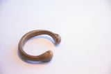 The C-shaped opening and solid, rounded ends of the antique African cuff bracelet.