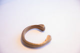 Aged patina on the smooth, C-shaped curve of an antique African snake cuff.