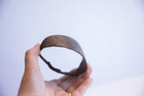 Hand holding vintage African bracelet, showing its dark, patinated metal texture and curved form.