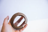 A hand holding a vintage African cuff, showing its curved interior and aged patina.