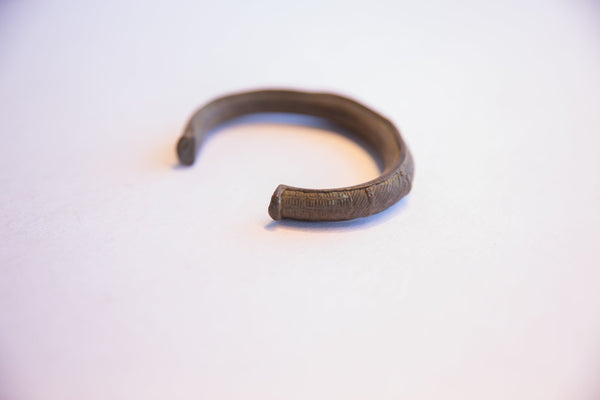 The open design of a vintage African cuff bracelet with a dark, textured patina.