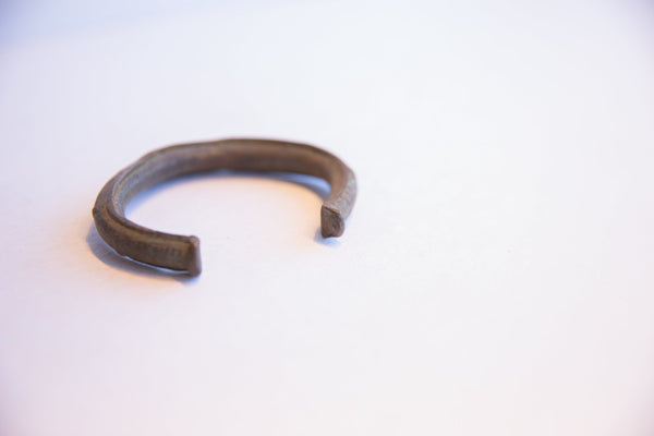 The open profile and rustic handmade texture of a vintage African currency bracelet.