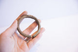 A hand holding the vintage African cuff bracelet, showing its scale and ribbed texture.