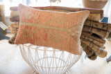 Textured vintage rug fragment pillow featuring a soft peach and muted green stylized pattern.