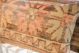 Vintage rug fragment pillow with aged hand-knotted geometric patterns, muted coral and tan.