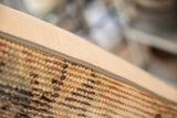 Textured side seam of vintage rug fragment pillow with beige woven backing.