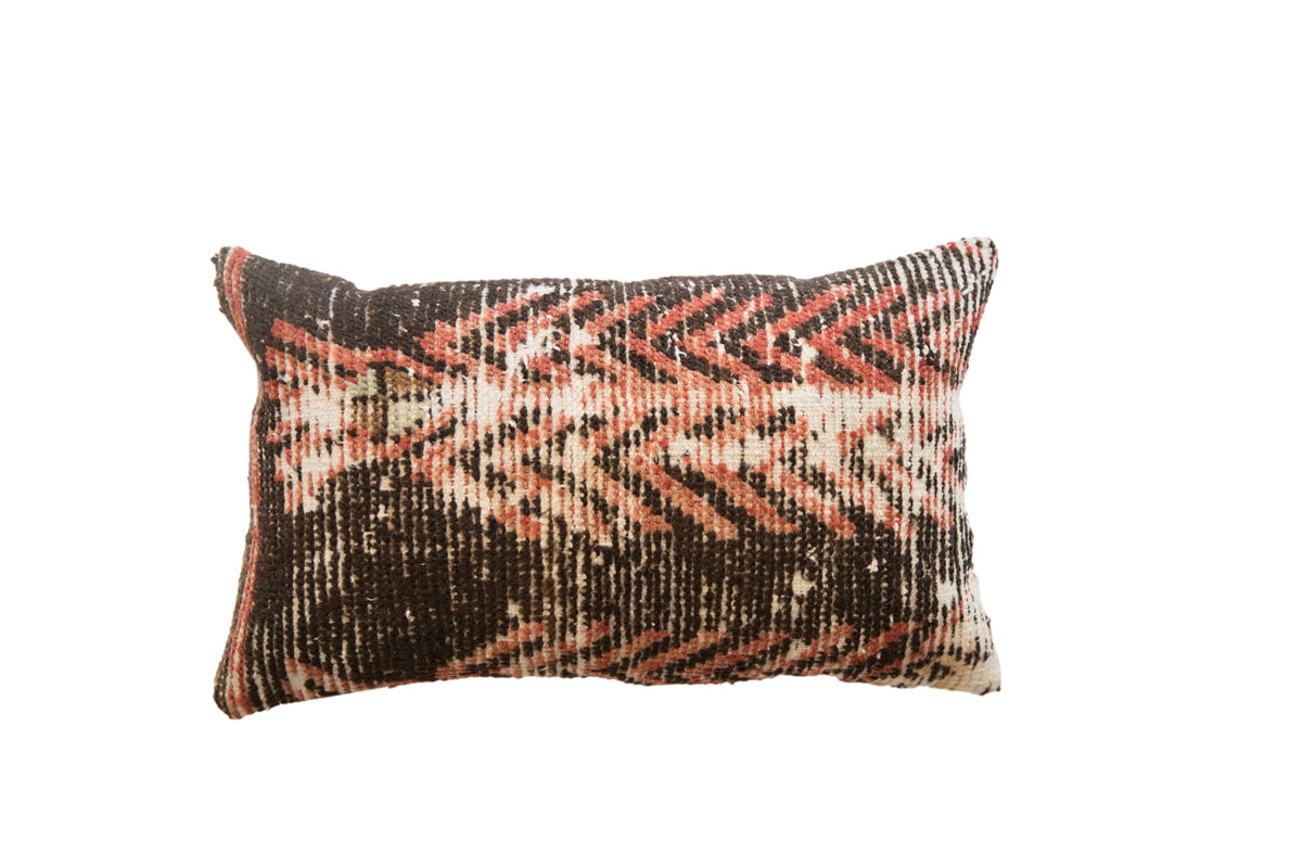 Rectangular vintage rug fragment pillow with a woven geometric pattern in brown, salmon, and ivory.