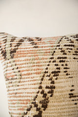 Textured weave of a vintage rug pillow with peach, sage, and brown geometric details.