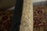 Seam detail of a vintage rug pillow showing the handwoven fragment and dark fabric backing.