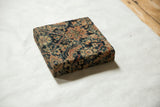The side profile of a decorative cork board wrapped in a textured antique Fereghan rug fragment.
