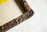 Corner detail of the decorative cork board, showing the antique rug fabric wrapped frame construction.