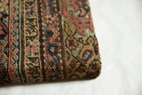 Close-up of the antique rug fragment's corner, highlighting its woven texture and wrapped edge.