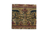 Antique Kerman rug fragment art on a cork board with symmetrical Art Nouveau floral motifs in tan, blue, and red.