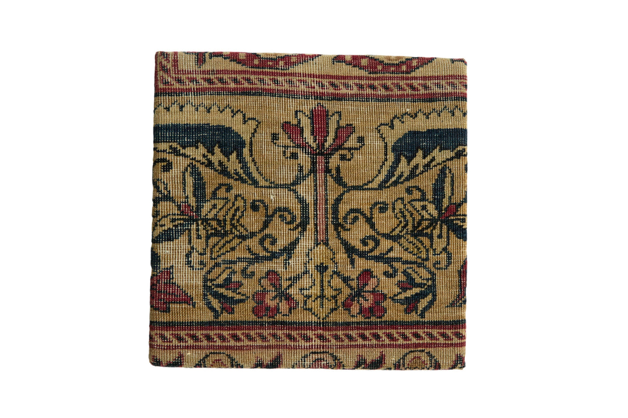 Antique Kerman rug fragment art on a cork board with symmetrical Art Nouveau floral motifs in tan, blue, and red.