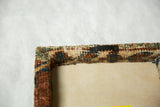 Back corner of the rug fragment art showing the sawtooth hanger and wrapped textile construction.
